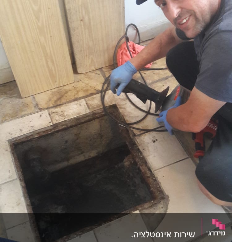 אדם עם כפפות וכלי עבודה ליד פתח ביוב